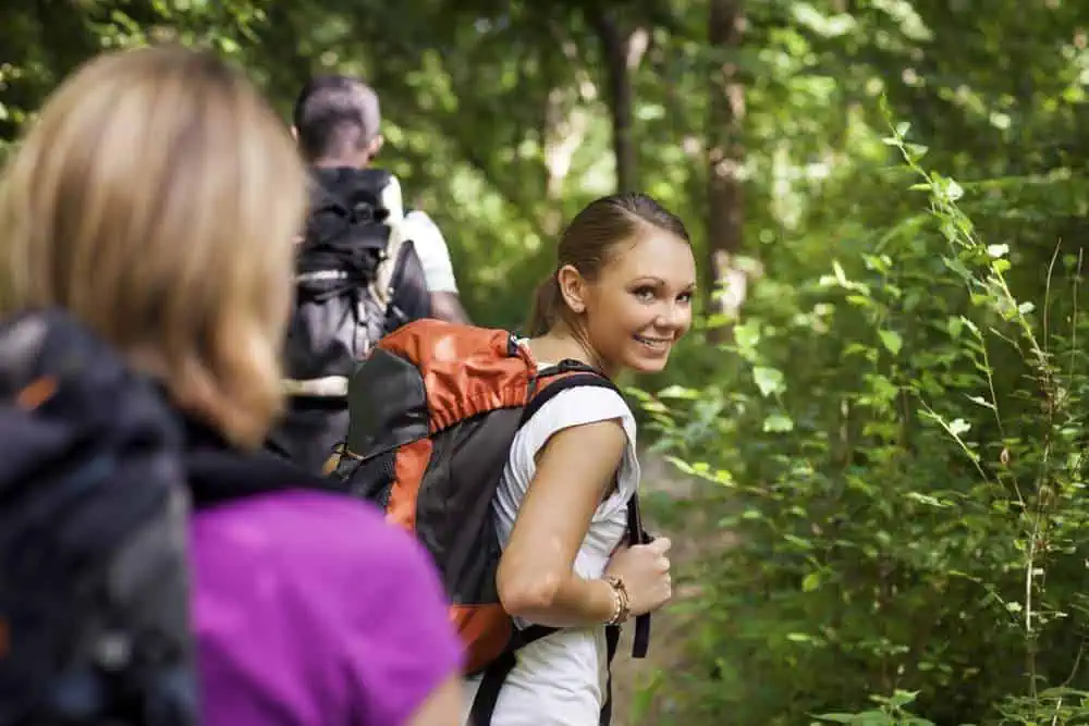 Women during hiking excursion in woods, with woman looking at camera over shoulders and smiling.
